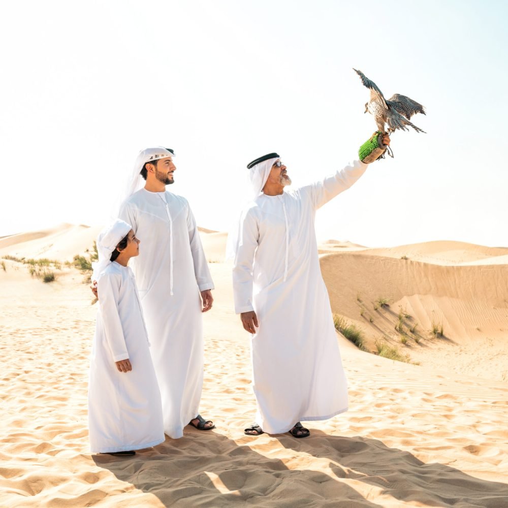 Three generation family making a safari in the desert of Dubai. Grandfather, son and grandson spending time together in the nature and training their falcon bird.